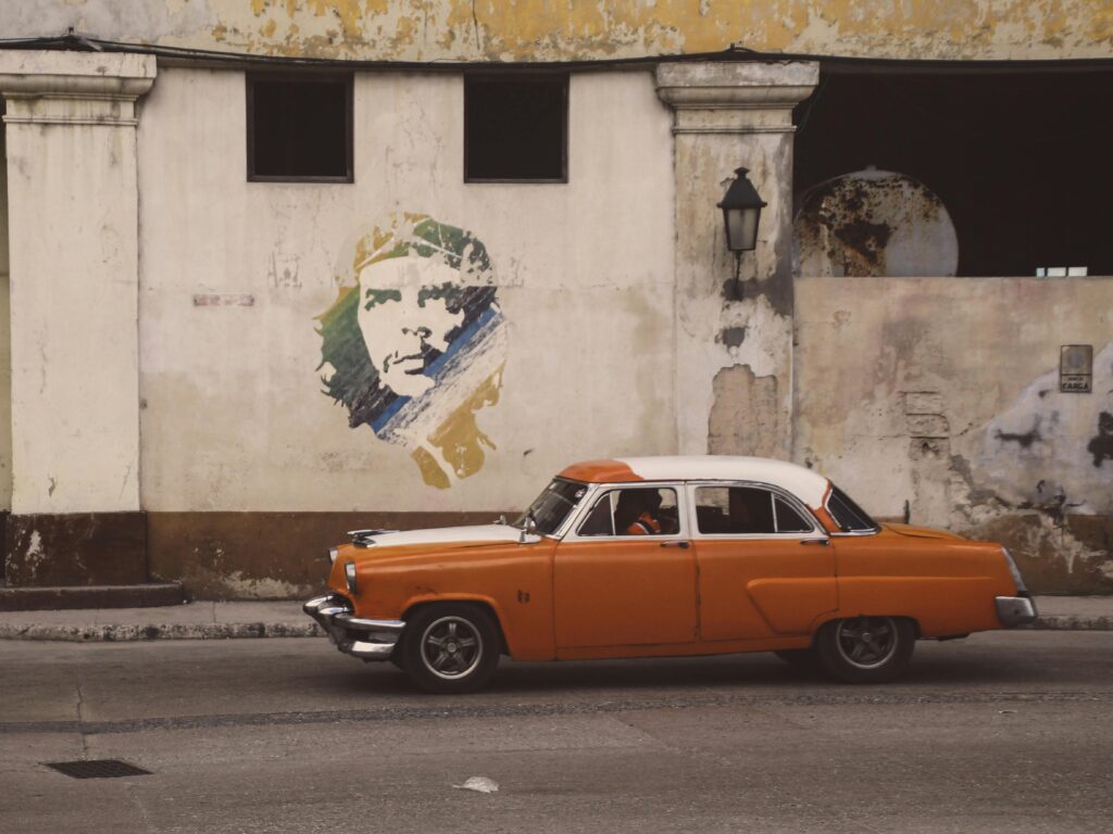 Vintage car driving past Che Guevara mural in Havana Cuba illustrating the long-term impact of economic sanctions on Cuban society and infrastructure