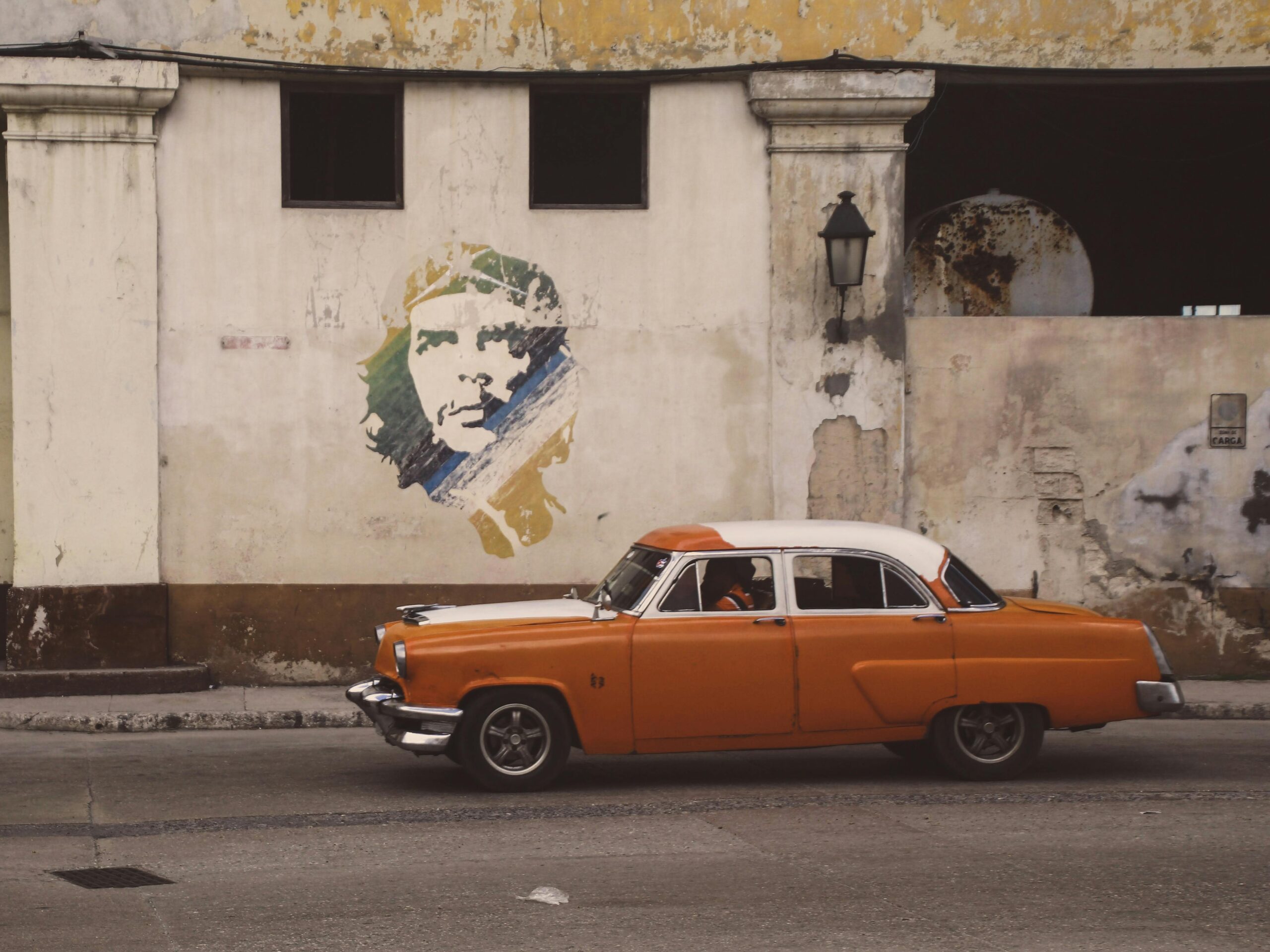 Vintage car driving past Che Guevara mural in Havana Cuba illustrating the long-term impact of economic sanctions on Cuban society and infrastructure